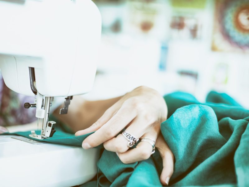 person sewing green textile using white electric sewing machine